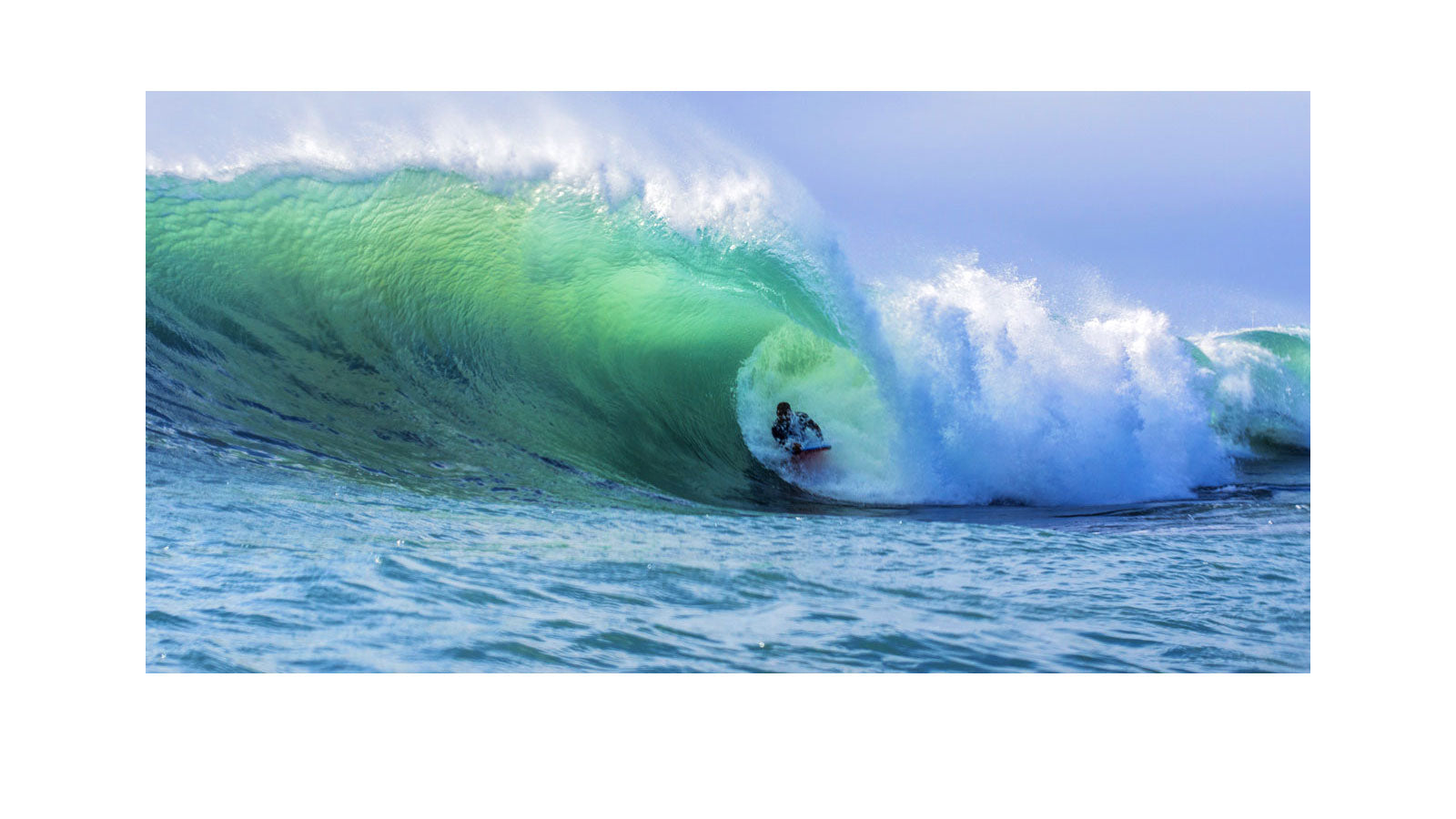 A bodyboarder riding deep inside a large green barrelling wave, tucked into the tube on a red bodyboard with white water breaking over the lip