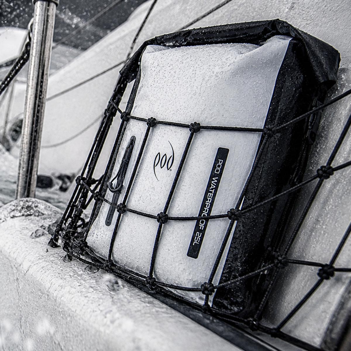 The POD Waterproof 25L backpack in white secured in a deck net on a wet sailing vessel in rough conditions, with water spray visible across the hull