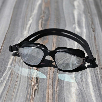 POD AquaLuxe Black Max swim goggles with silver mirror lenses and black frame resting on a stone surface in natural light