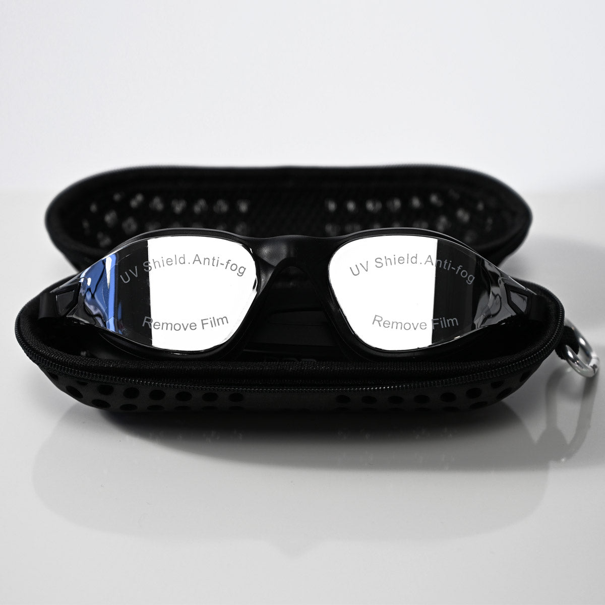 Black swim goggles with reflective silver lenses resting inside an open black zippered carrying case on a light gray reflective surface.