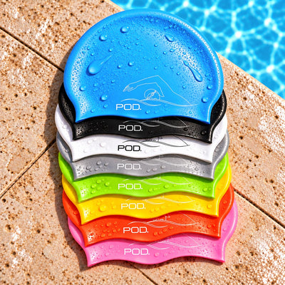 A stack of six POD. swim caps in blue, black, white, green, yellow, orange, and pink, shown on a pool deck with pool water in the background.