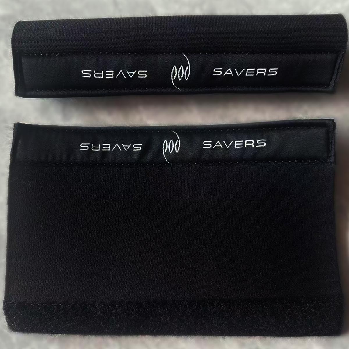 Two black neoprene Rubber Swim Fin Strap Heel Pads and Ankle Protection with white 'SAVERS' and 'POD' branding, displayed on a light gray textured background.