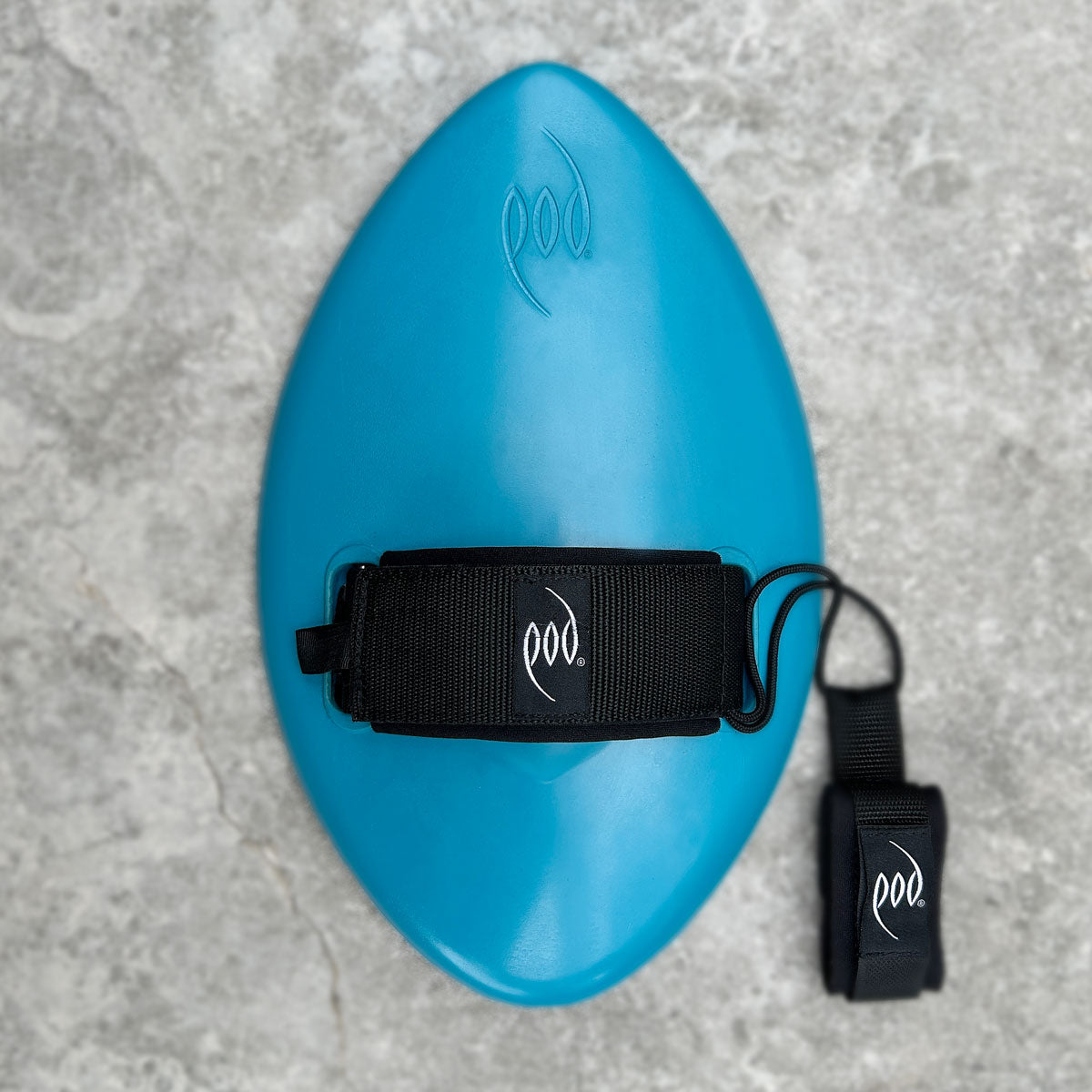 A bright blue body surfing board with a black hand strap and matching black wrist strap, both featuring a white 'pod' logo, laid flat on a grey stone textured surface.