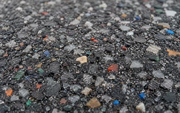 Close-up of road surfacing material showing recycled plastic and glass fragments visibly integrated into asphalt - demonstrating recycled content in road construction